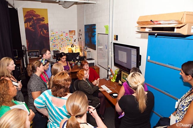 A group of people sitting at a desk in front of a crowd, disney animation research library