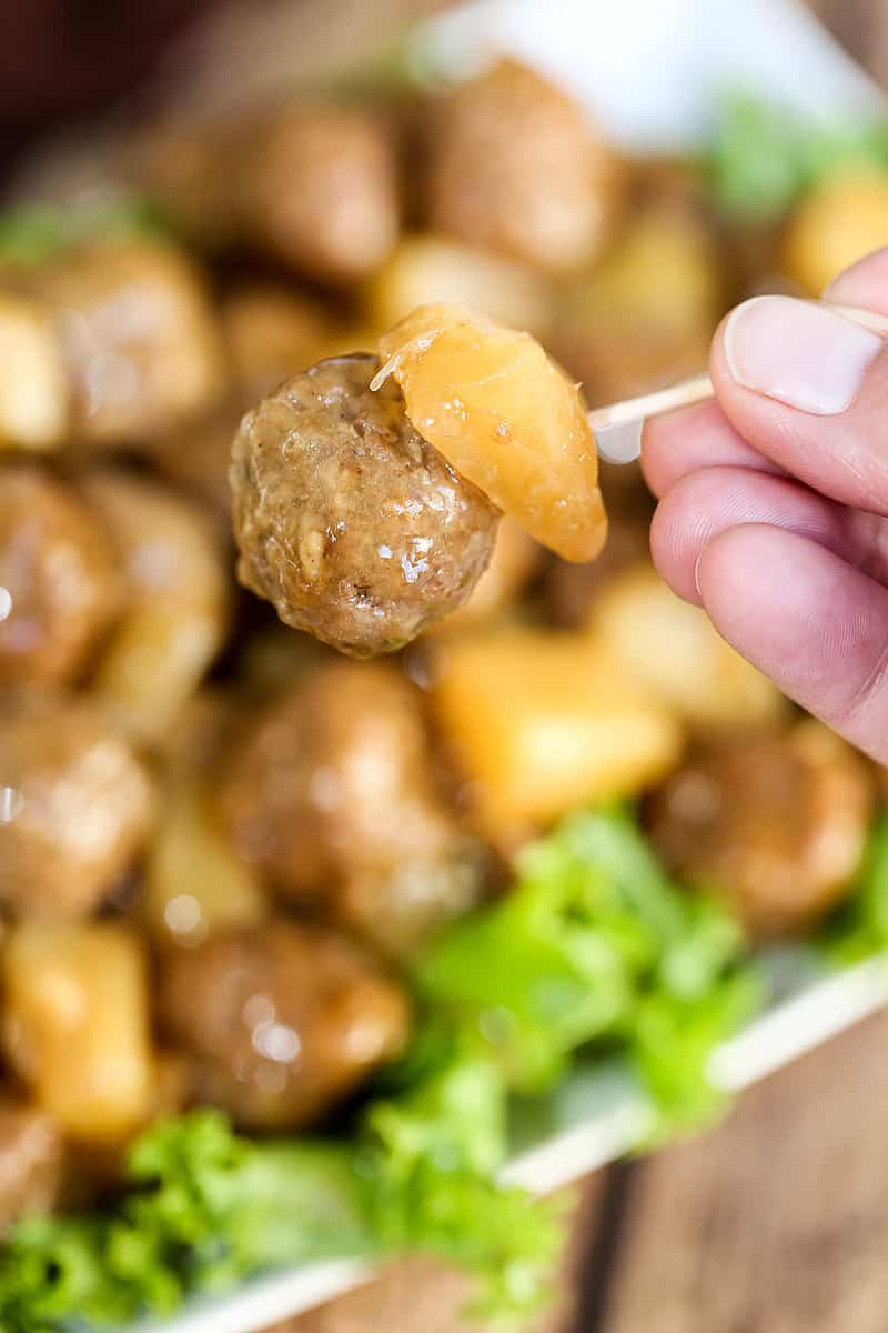 A close up of a person holding food, with Meatball and pineapple