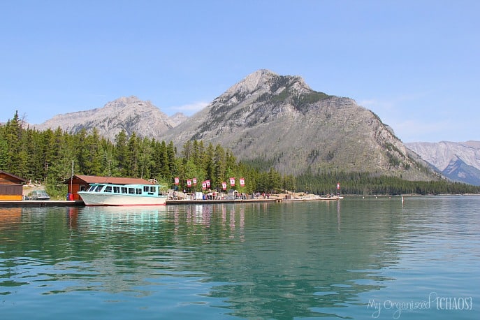 A small boat in a body of water with a mountain in the background, lake minnewanka