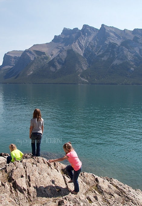 A group of people on a rock next to a body of water, lake minnewanka