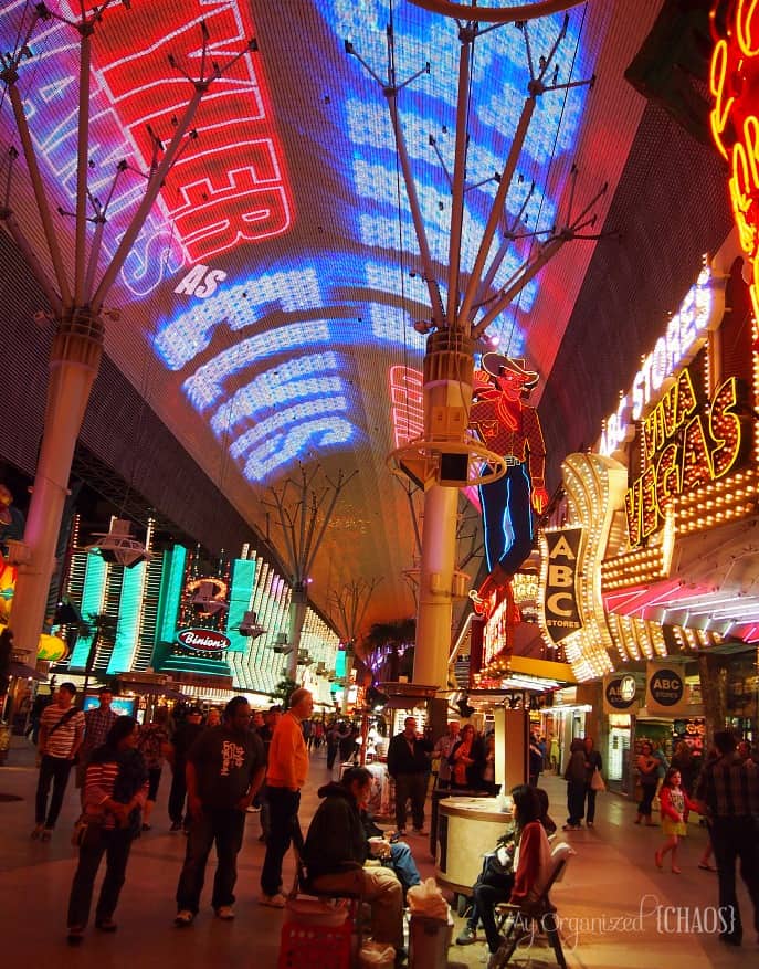A group of people walking in front of a store with Fremont Street Experience in the background