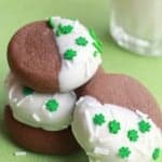 chocolate cookies half dipped in white chocolate with clover leaf sprinkles on a napkin.