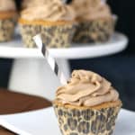Root beer cupcakes with brown root beer frosting and a straw inserted on top, on a white plate.