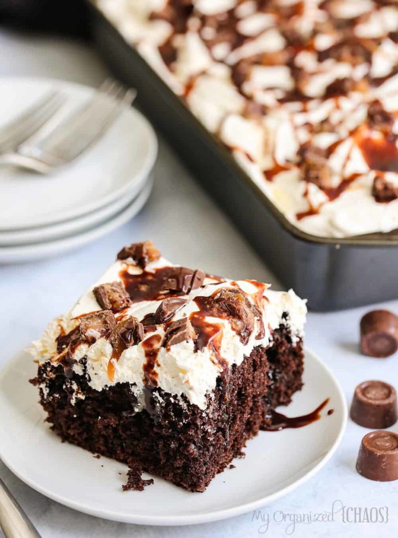 A piece of chocolate cake on a plate, with Poke Cake and whipped Cream and rolo chocolate