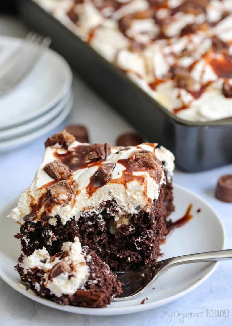 A piece of poke cake on a plate, with Chocolate and Caramel and whipped cream