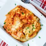lasagna on a white plate with fresh parsley sprinkled on top, and a fork beside it.