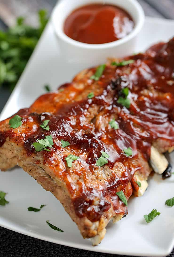 A close up of a plate of food with a slice of pizza, with Ribs and Sauce