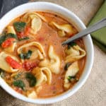 A bowl of food on a plate, with Soup and Tortellini