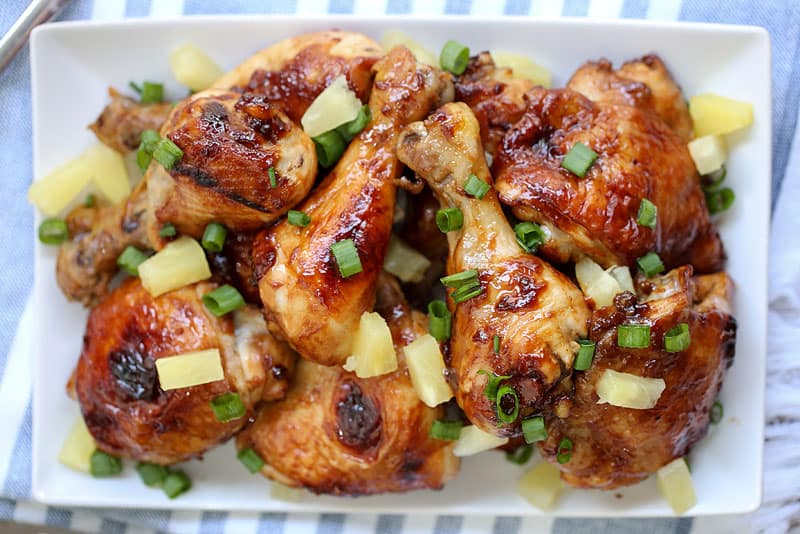 A close up of a plate of food, with Chicken legs and pineapple