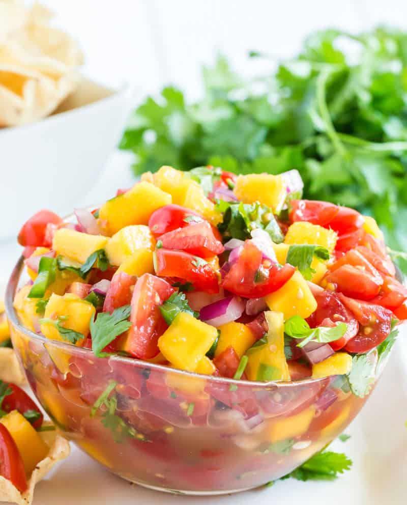 A bowl of food on a plate, with Mango and Tomato