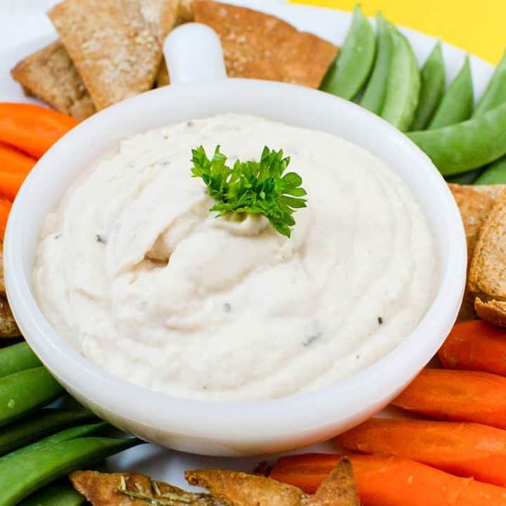 hummus in a bowl surrounded by fresh vegetable sticks and pita chips