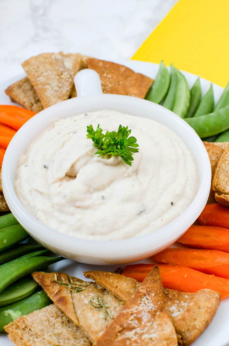 hummus in a bowl surrounded by fresh vegetable sticks and pita chips