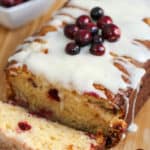 Sliced Cranberry Eggnog Bread on a table with fresh cranberries beside it, and eggnog icing on top.