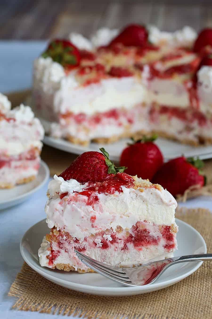a slice of strawberry shortcake ice cream cake on a plate with the whole cake in the background