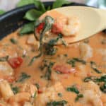 tuscan shrimp on a wooden spoon being lifted from a skillet