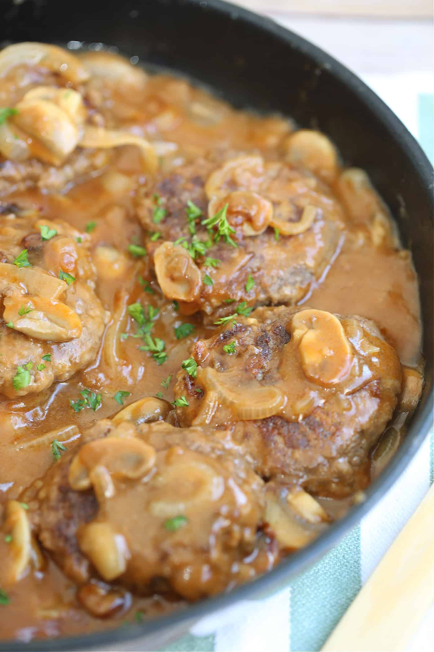 salisbury steak in a frying pan with mushrooms and onions