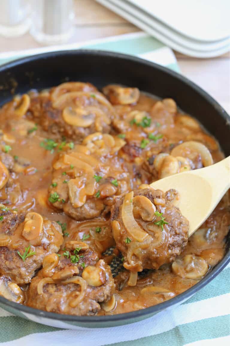 salisbury steak in a frying pan being lifted with a wooden spoon