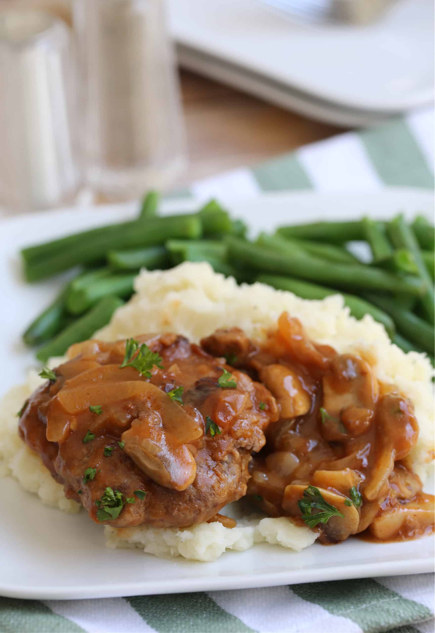 salisbury steak on a plate with mashed potatoes and green beans