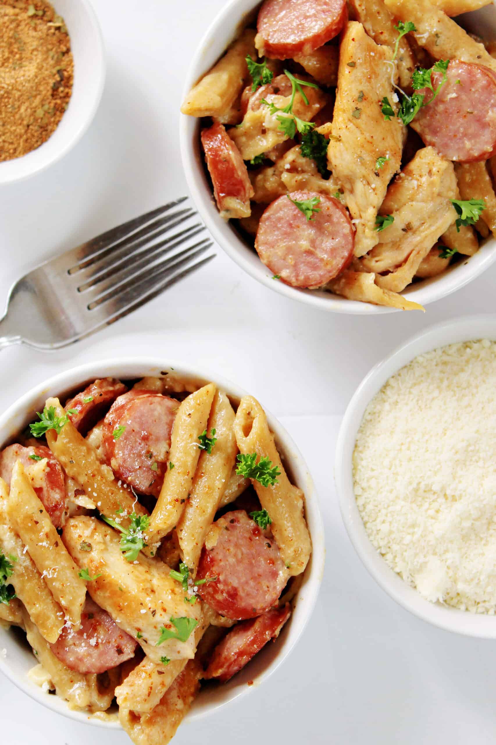 cajun chicken alfredo pasta with sausage in two white bowls with forks