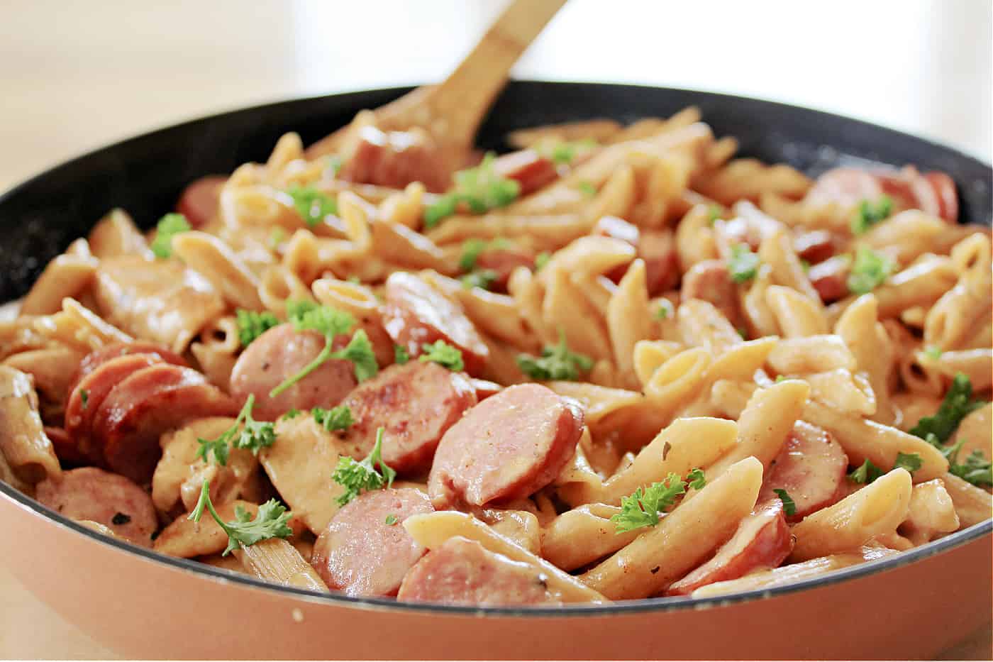 chicken sausage and pasta in a skillet with a wooden spoon