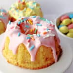 a mini bundt cake with pink icing and sprinkles on a cupcake stand.