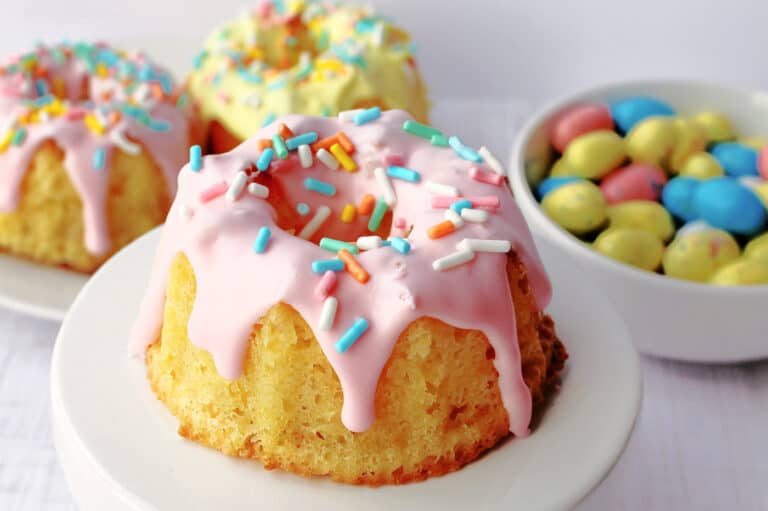 a mini bundt cake with pink icing and sprinkles on a cupcake stand.