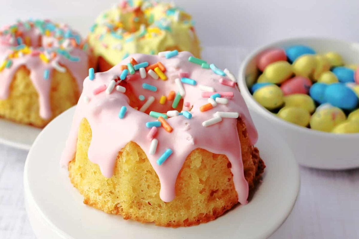 a mini bundt cake with pink icing and sprinkles on a cupcake stand.