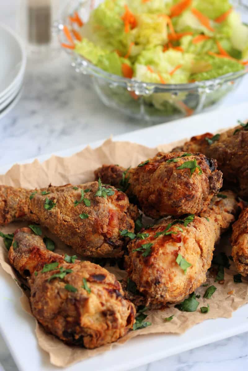 pieces of fried chicken drumsticks on a white plate with a bowl of salad and plates