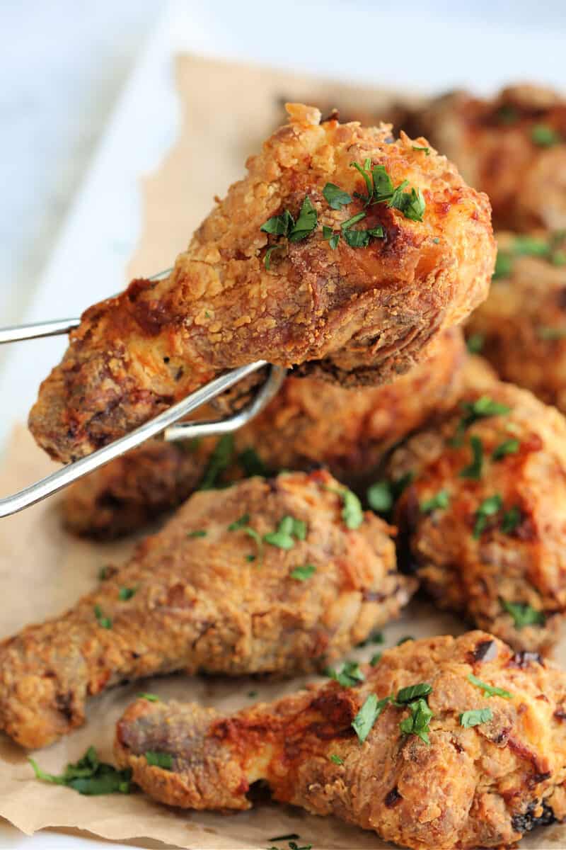 a piece of fried chicken being picked up by tongs over a plate of fried chicken pieces