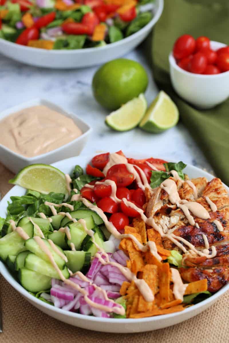 bbq chicken salad in a bowl with dressing drizzled on it with lime and dressing in the background