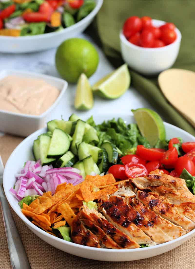 bbq chicken salad in a bowl with lime wedges on a table with another salad in a bowl in the back