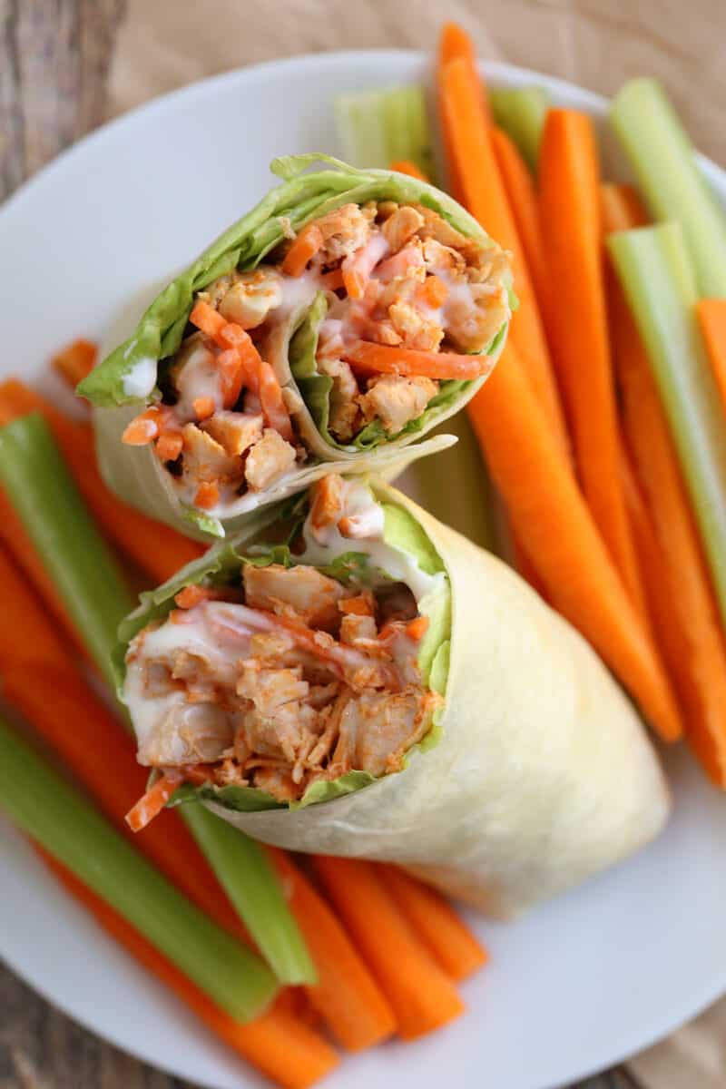 two chicken wraps on a plate surrounded by cut raw vegetables