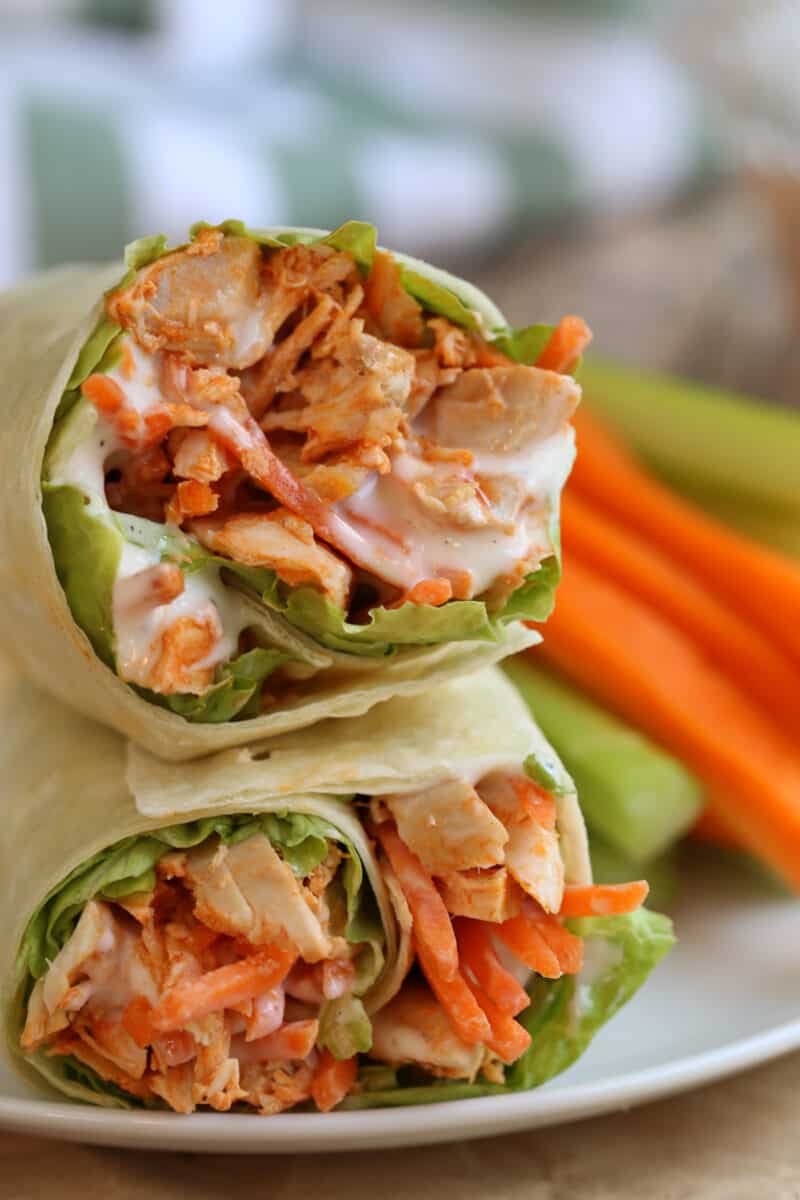 two stacked buffalo chicken wraps beside cut vegetables