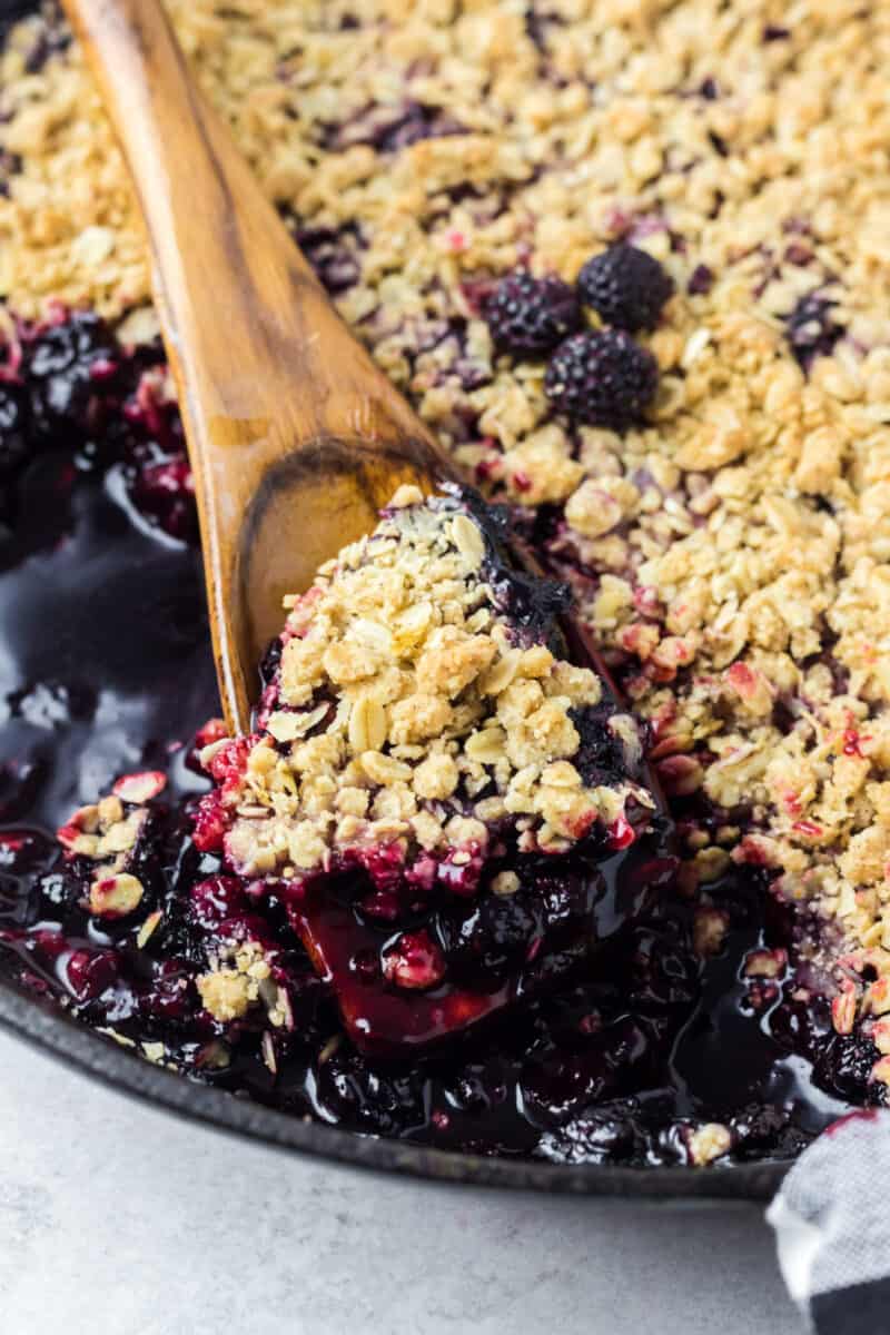 a cast iron pan with berry crisp inside and a wooden spoon