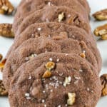 a pile of chocolate chip cookies on a white tray with pecans