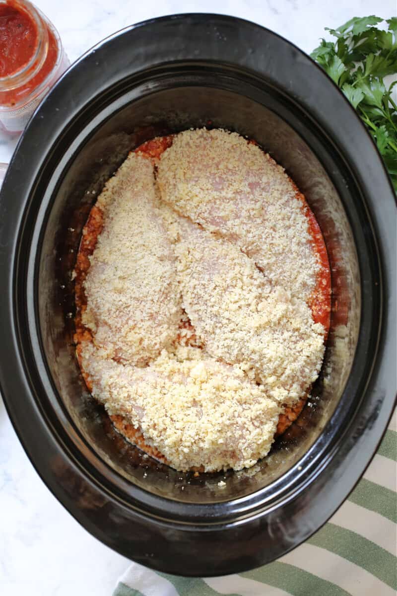 breaded chicken breasts on marinara in a black slow cooker