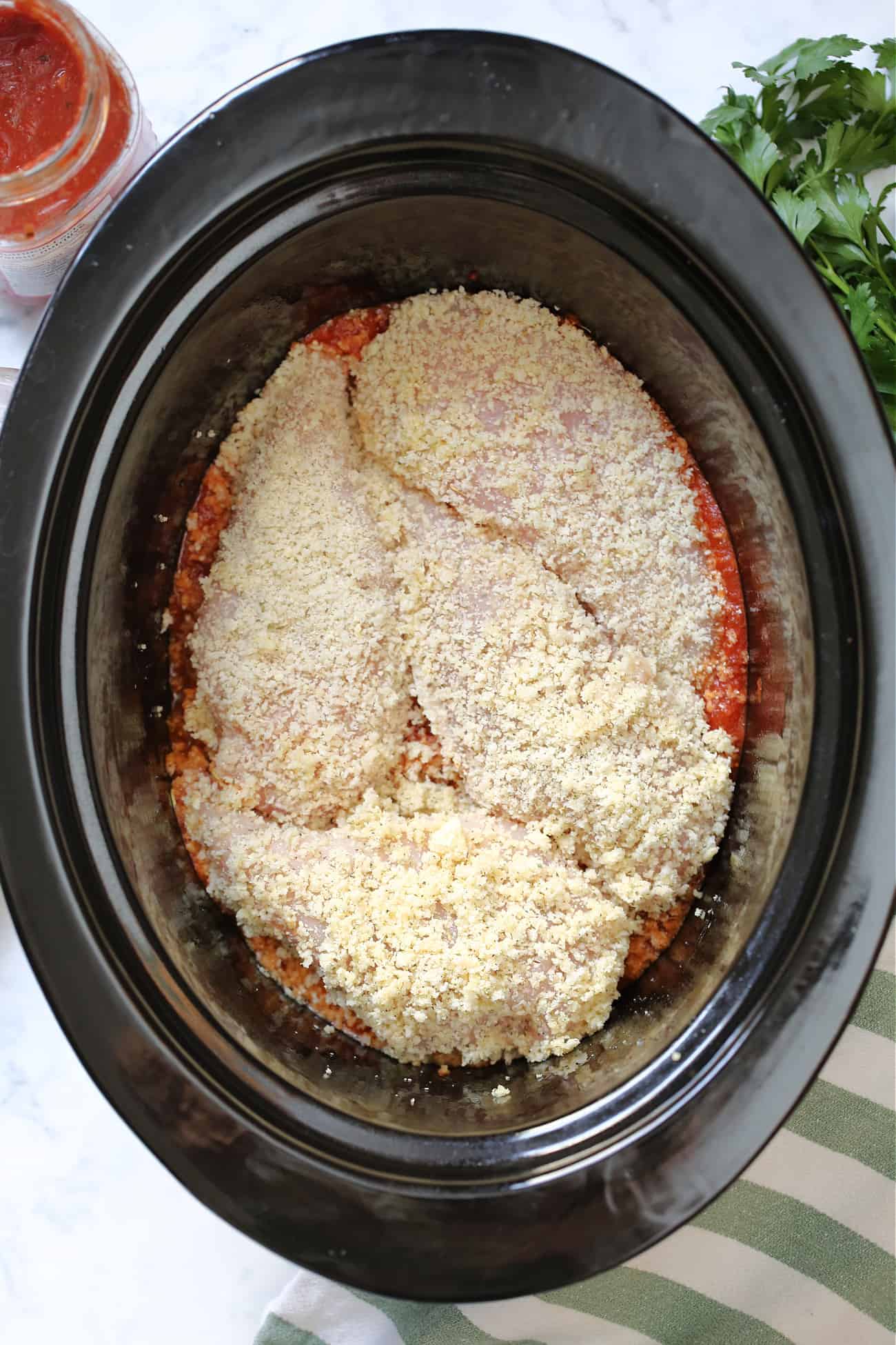 breaded chicken breasts on marinara in a black slow cooker