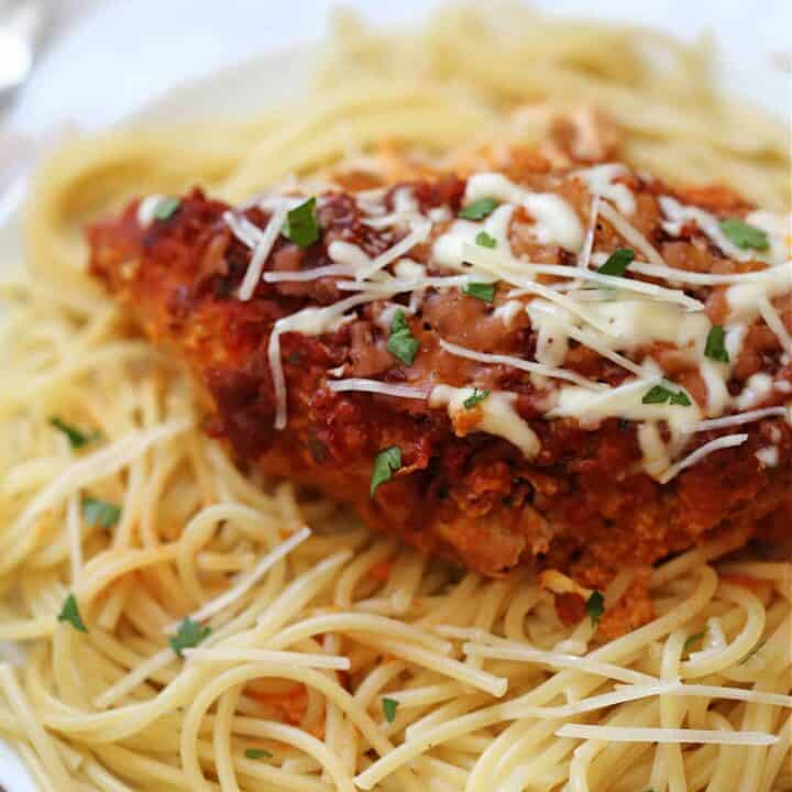a whole piece of chicken parmesan on top of spaghetti on a white plate
