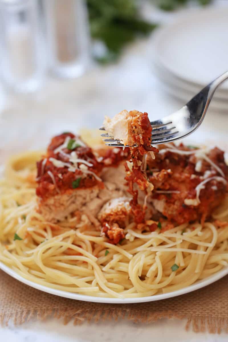 chicken parmesan and spaghetti being lifted by a fork on a white plate