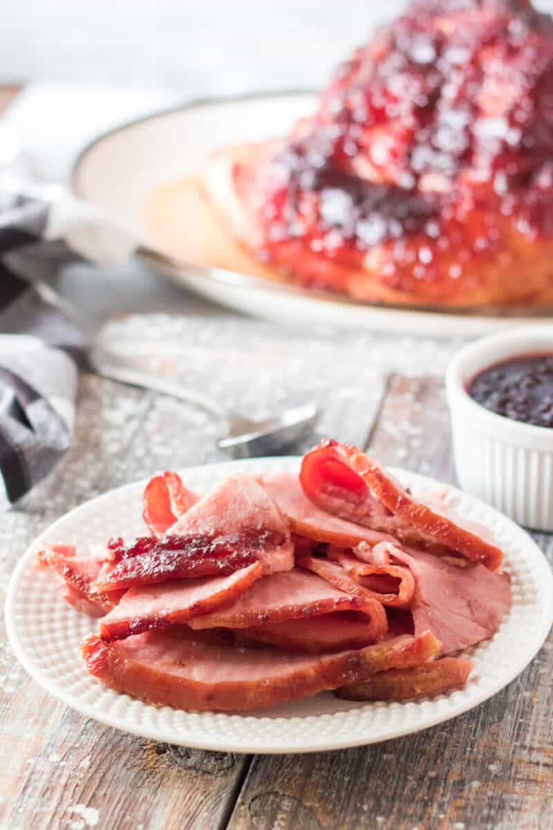 slices of holiday ham on white plate with whole ham in background
