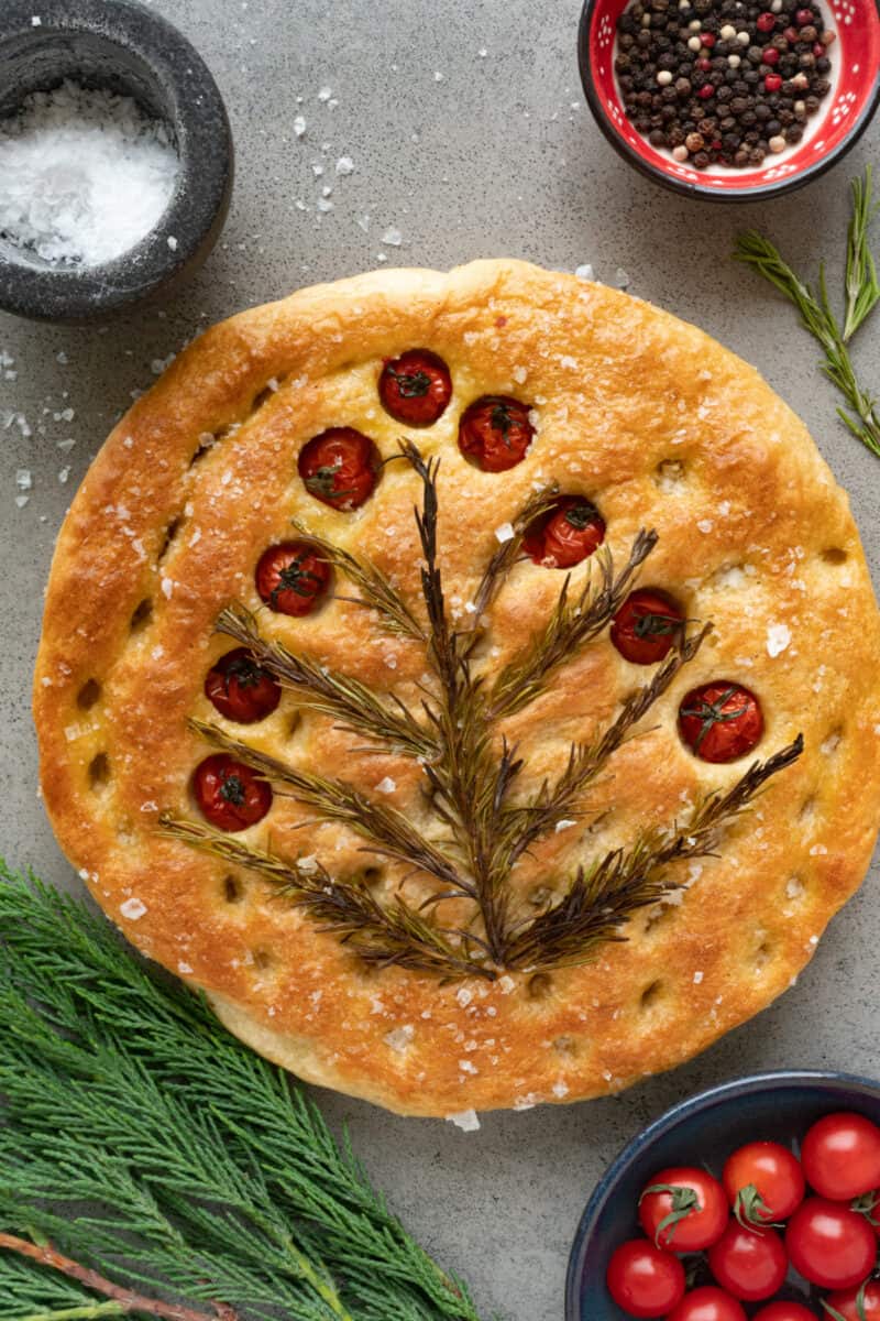 a round focaccia bread on the table with fresh ingredients around it