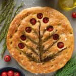 focaccia bead with rosemary and tomatoes baked on top on a table with fresh ingredients