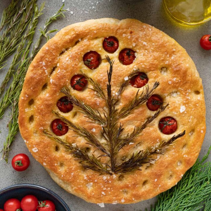 focaccia bead with rosemary and tomatoes baked on top on a table with fresh ingredients