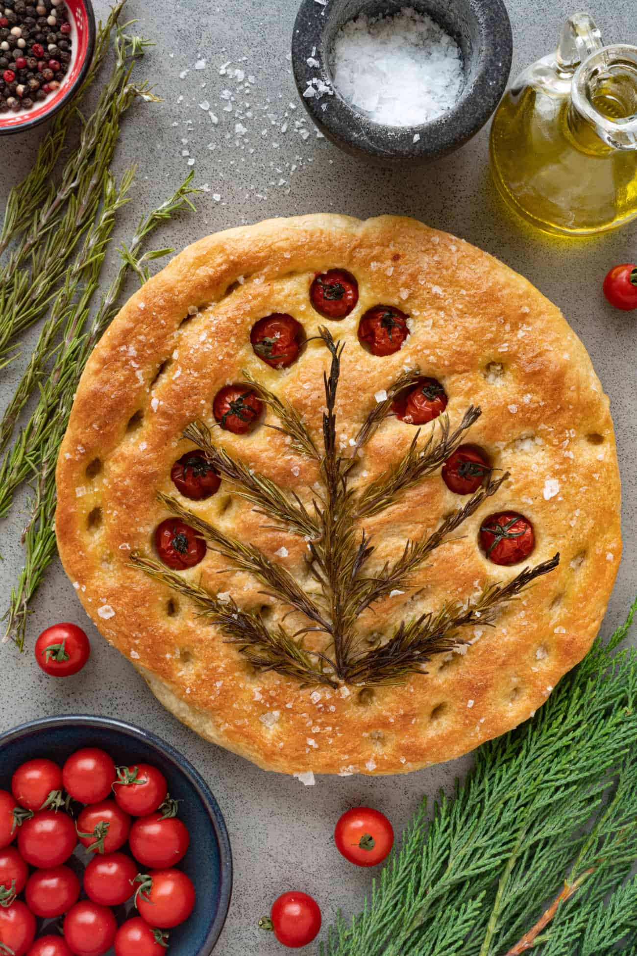 focaccia bead with rosemary and tomatoes baked on top on a table with fresh ingredients