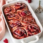 raspberry cinnamon rolls in a white baking dish on a table.