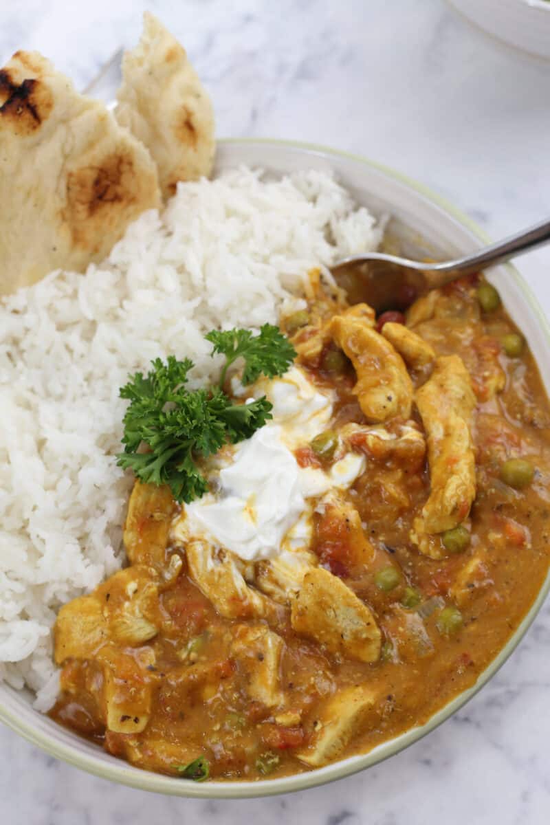 a bowl of chicken curry alongside rice and naan bread