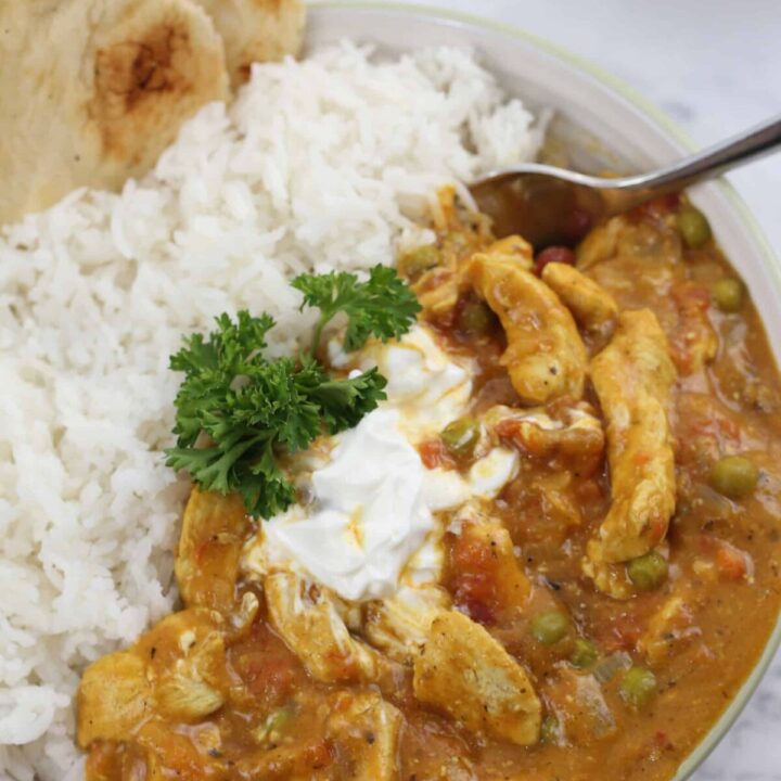 a bowl of chicken curry alongside rice and naan bread