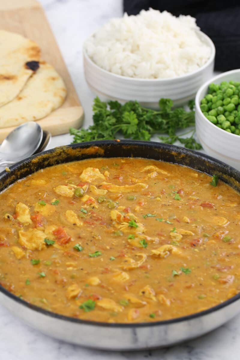 chicken curry in a large skillet with rice, peas and naan flatbread beside it