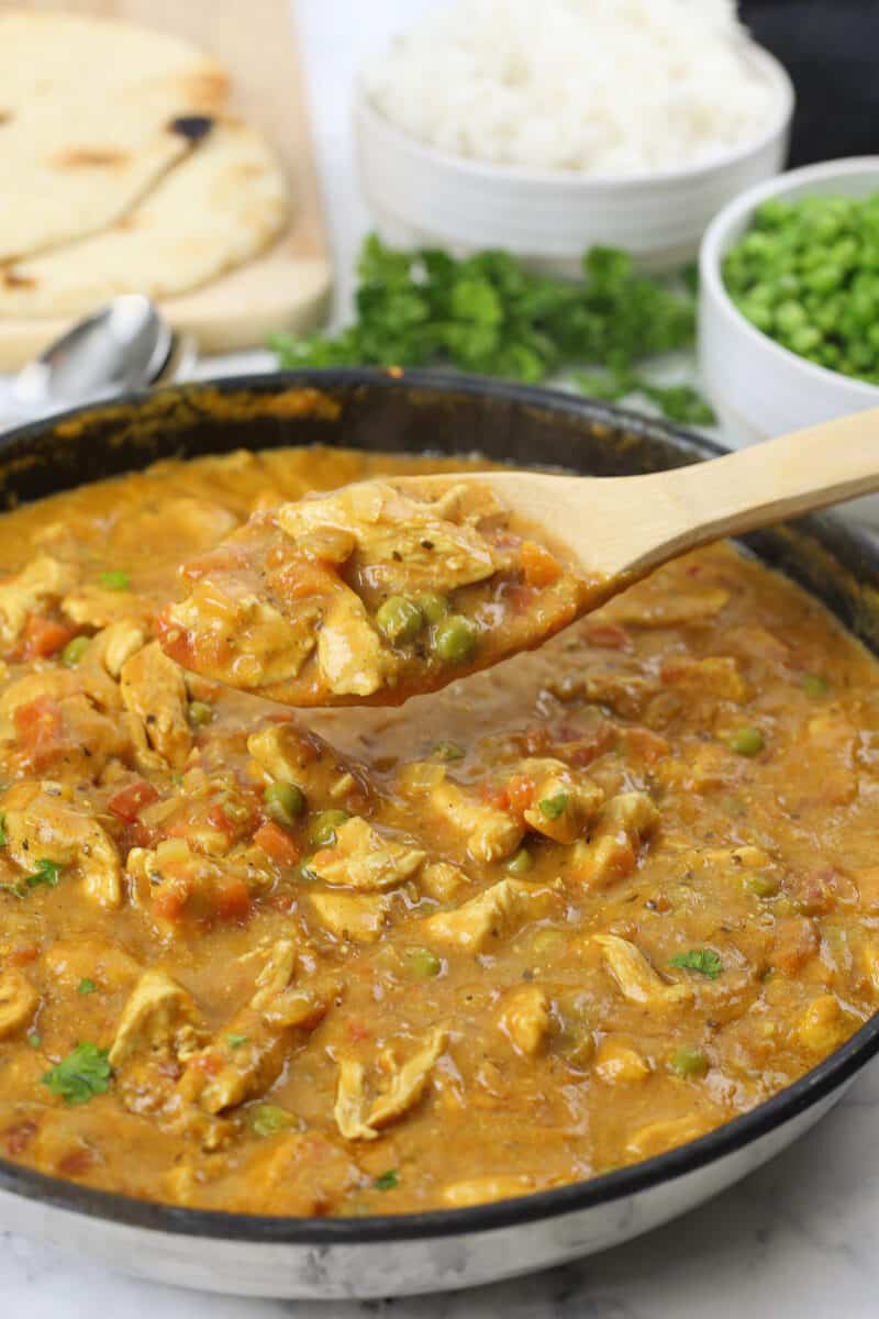 chicken curry being lifted out of a large skillet by a wooden spoon