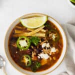 a bowl of chicken tortilla soup with a lime wedge and tortilla strips on top